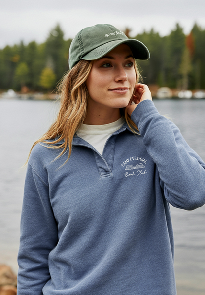 Woman wearing a blue pullover and green cap by a lake with trees in the background