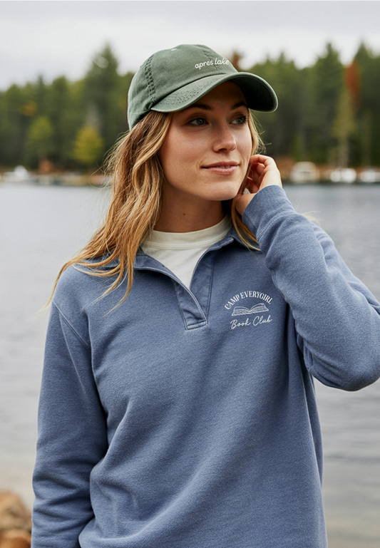 Woman wearing a blue pullover and green cap by a lake with trees in the background